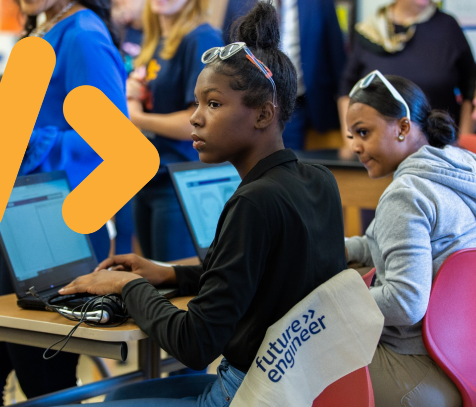 Deux lycéennes prennent des notes sur leur ordinateur. Un symbole de code jaune encadre la photo.
