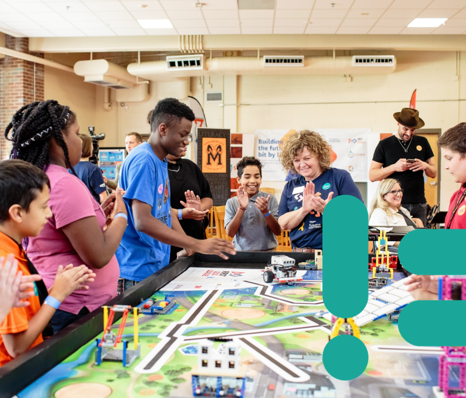 Des collégiens applaudissent un des élèves qui a réussi à faire rouler une voiture automatisée. Un symbole de code vert apparaît à gauche de la photo.