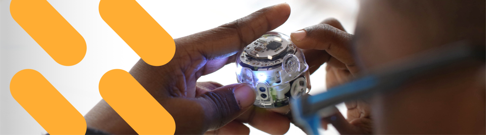 A boy plays with a small robot. There are orange slash code symbol graphics overlaid on the image.